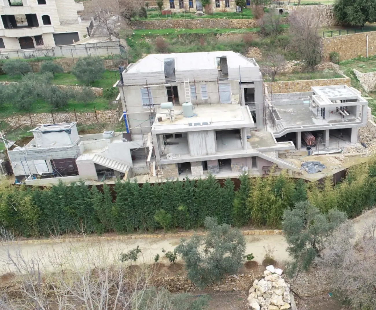 Group Four reinforced concrete frame under construction on a sloped plot in Bkassine, Chouf, Lebanon, with stone retaining walls